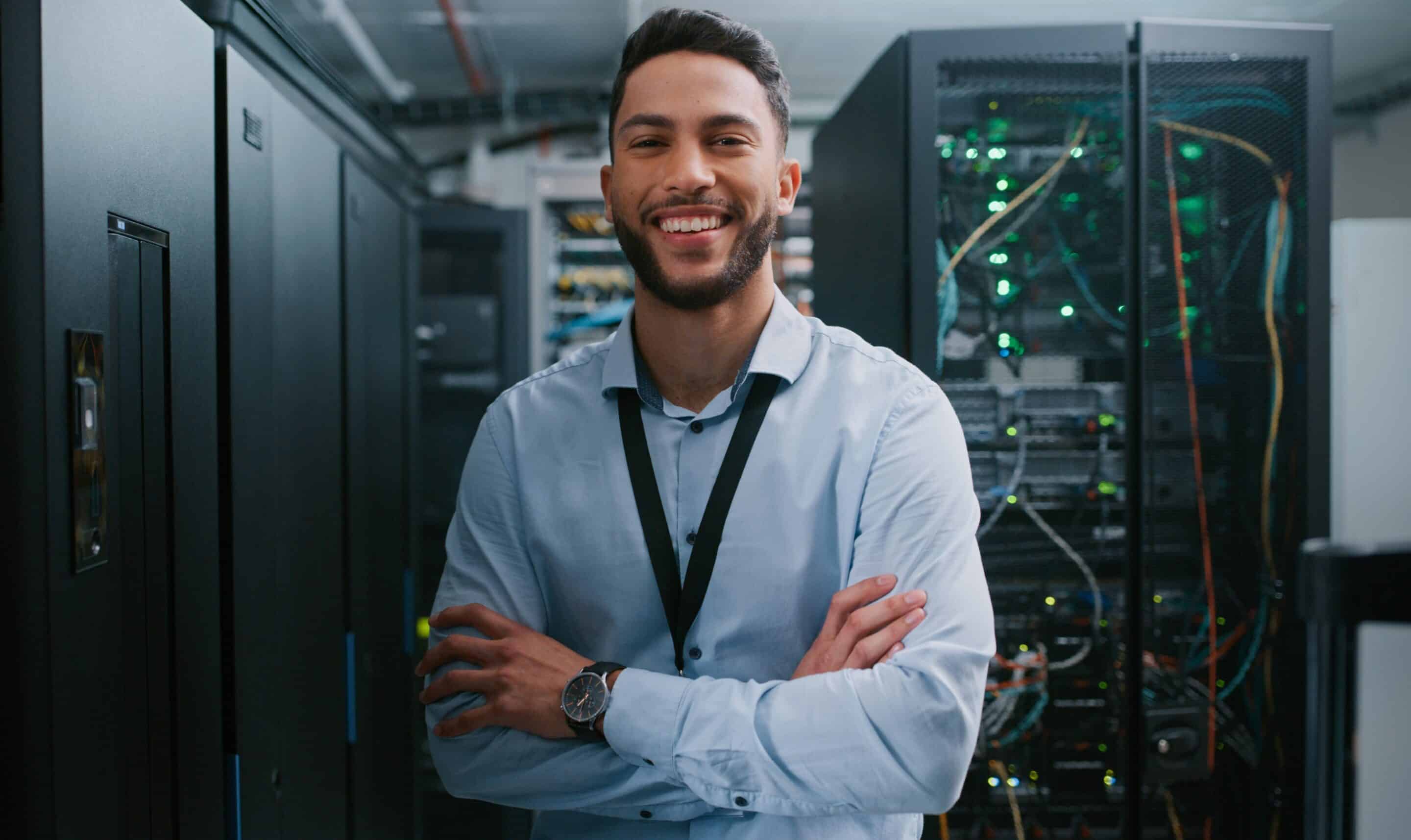 A Montreal IT consultant stands in front of IT hardware with his arms crossed confidently